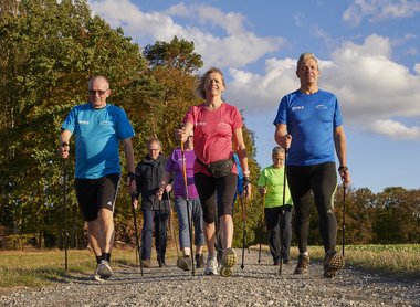 Eine Gruppe von Erwachsenen, die im Sonnenschein Nordic Walking machen.