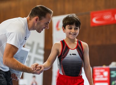 Ein Junge wird von seinem Trainer beim Turnen ermutigt.