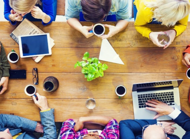 Eine Gruppe Menschen sitzt mit Laptops und Kaffee an einem Tisch und hat ein Meeting.