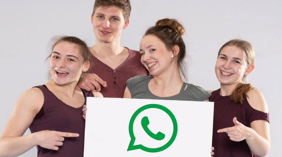 Eine Gruppe von jungen Menschen, die sich freuen und ein Schild mit dem WhatsApp-Logo hochhalten.