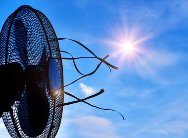 Auf dem Bild ist ein Ventilator vor blauem Himmel und strahlender Sonne abgebildet.